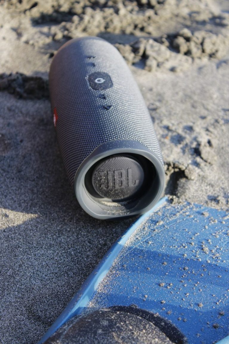 Gray JBL Bluetooth speaker resting on sandy beach in Santa Marta, Colombia, capturing a casual outdoor vibe.