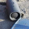 Gray JBL Bluetooth speaker resting on sandy beach in Santa Marta, Colombia, capturing a casual outdoor vibe.